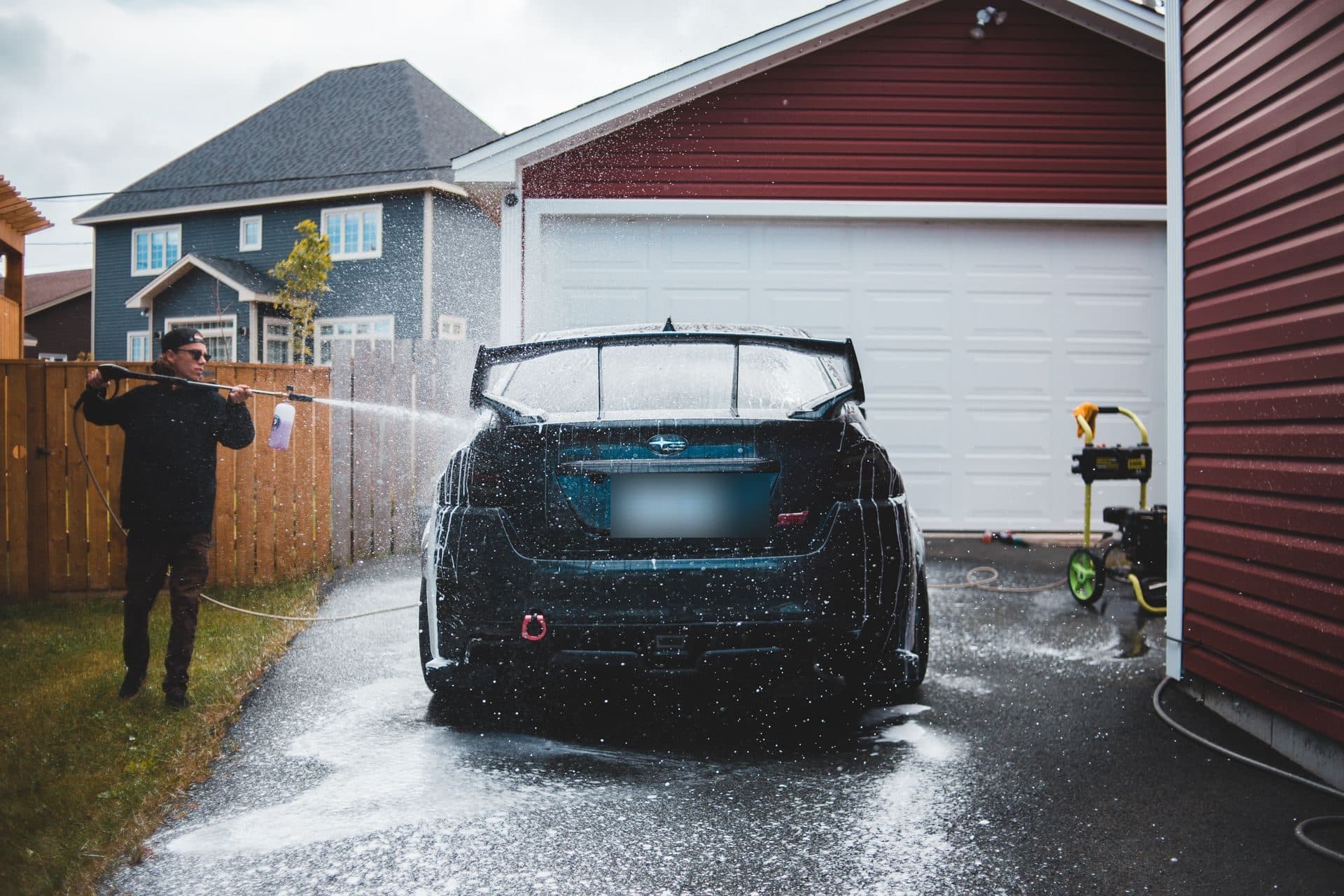 A detailer pressure-washing a car in a driveway